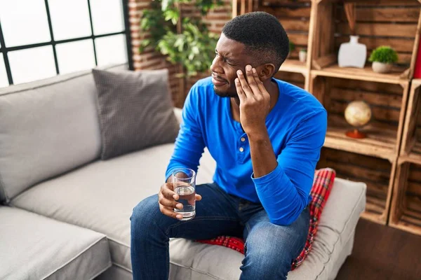 stock image Young african american man with headache holding glass of water at home