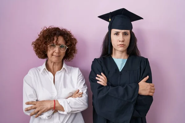 ヒスパニック系の母親と娘が卒業キャップと式のローブを着て懐疑的で緊張し 両腕を組んで顔に不承認の表現 否定的な人 — ストック写真