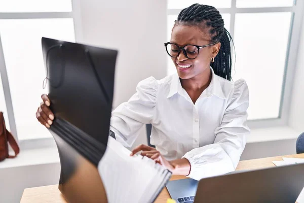 アフリカ系アメリカ人女性ビジネスワーカーがオフィスでノートパソコンを使ってバインダーを開ける — ストック写真