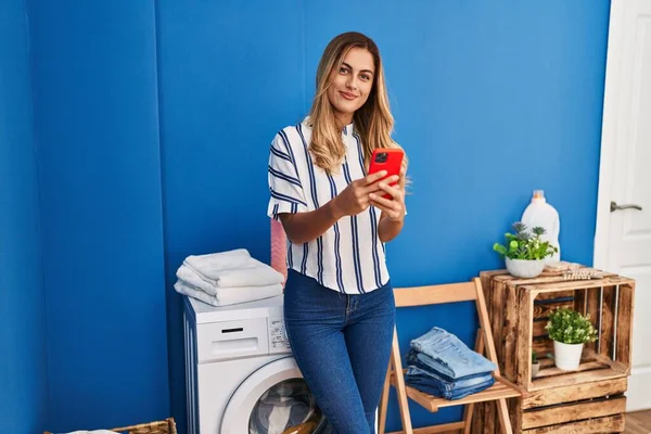 Ung Blond Kvinna Med Smartphone Väntar Tvättmaskin Tvättstugan — Stockfoto
