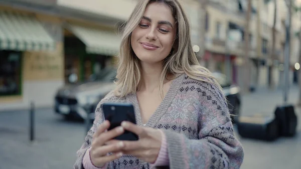 若いですブロンド女性笑顔自信を持って使用してスマートフォンでストリート — ストック写真