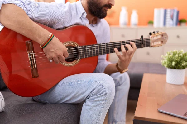 Young hispanic man having online guitar class sitting on sofa at home