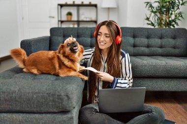 Genç İspanyol kadın dizüstü bilgisayar kullanıyor. Evde köpekle oturuyor.