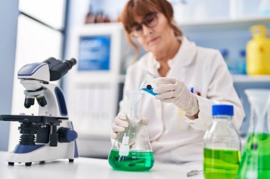 Laboratuvarda sıvı ölçümü yapan orta yaşlı kadın bilim adamı.