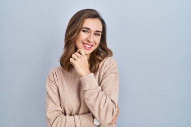 İzole edilmiş arka planda duran genç bir kadın kameraya kendinden emin bir şekilde bakıyor kollarını kavuşturmuş ve çenesini kaldırmış gülümsüyor. Olumlu düşünmek. 