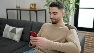 Young arab man using smartphone sitting on sofa at home