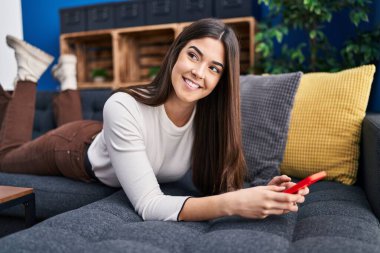 Evdeki kanepede uzanmış akıllı telefon kullanan genç, güzel İspanyol kadın.