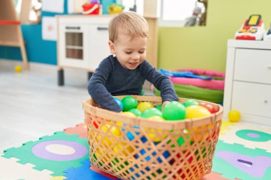 Anaokulunda yerde taşaklarıyla oynayan sevimli sarışın çocuk.