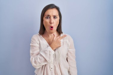 Mavi arka planda dikilen orta yaşlı İspanyol kadın parmağını yana çevirerek şaşırdı, ağzı açık hayret içinde kaldı.. 