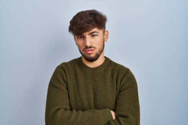 Arab man with beard standing over blue background skeptic and nervous, disapproving expression on face with crossed arms. negative person. 