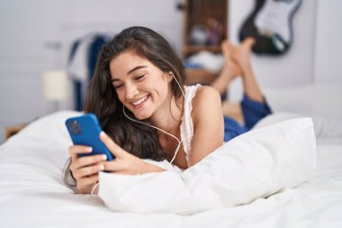 Young hispanic woman listening to music lying on bed at bedroom
