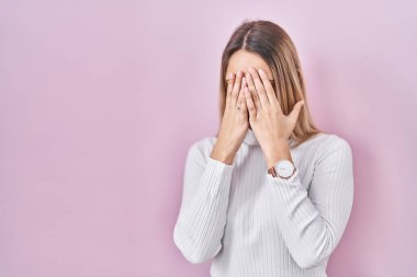 Pembe arka planda beyaz kazak giyen genç sarışın kadın. Ağlarken suratını ellerle kapatan üzgün bir ifade. depresyon kavramı. 