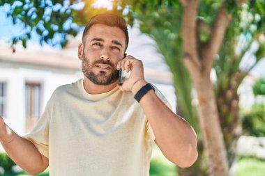 Young hispanic man talking on smartphone with serious expression at park