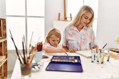 Mother and daughter smiling confident drawing on notebook at art studio