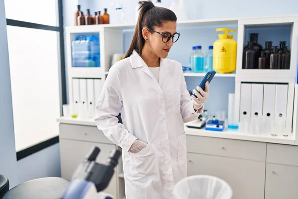 Νεαρή Ισπανίδα Που Φοράει Στολή Επιστήμονα Χρησιμοποιώντας Smartphone Στο Εργαστήριο — Φωτογραφία Αρχείου