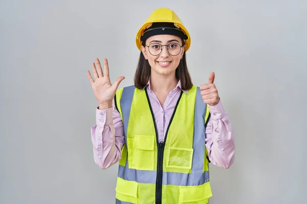 西班牙裔女孩身穿建筑工人制服 头戴安全帽 手握六号指尖 面带微笑 自信而快乐 — 图库照片