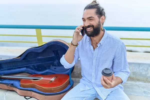 Young Hispanic Man Musician Talking Smartphone Drinking Coffee Seaside —  Fotos de Stock
