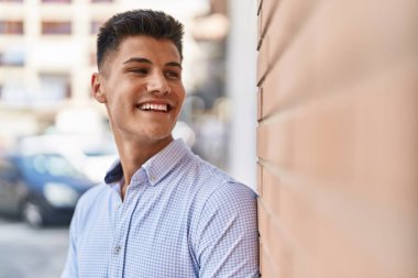 Young hispanic man smiling confident looking to the side at street