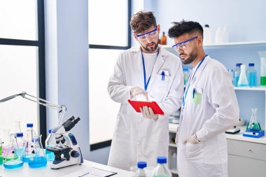 Young couple wearing scientist uniform using touchpad at laboratory
