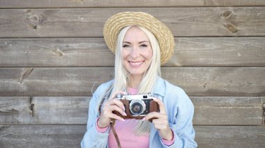 Young blonde woman tourist using vintage camera over isolated wooden background