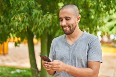 Parkta akıllı telefon kullanarak gülümseyen genç Latin adam.