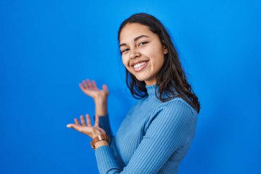 Mavi arka planda duran Brezilyalı genç kadın gülümseyerek doğal bir şekilde içeri girmeye davet ediyor. 