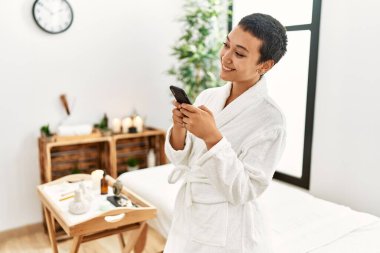Genç İspanyol kadın bornoz giyiyor güzellik merkezinde akıllı telefon kullanıyor.