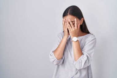 Young hispanic woman standing over white background with sad expression covering face with hands while crying. depression concept. 