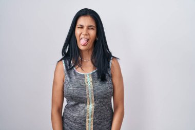 Beyaz arka planda dikilen olgun İspanyol kadın komik bir ifadeyle mutlu bir şekilde dilini dışarı çıkarıyor. duygu kavramı. 