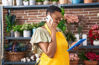 Çiçekçide dokunmatik ped kullanarak akıllı telefondan konuşan Afrikalı Amerikalı kadın çiçekçi.