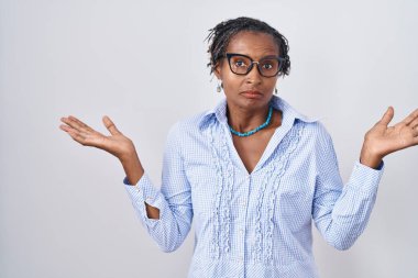 Beyaz arka plan üzerinde duran Afrikalı kadın gözlüksüz ve elleri ve kolları havada kafası karışmış bir ifade takınıyor. şüphe kavramı. 