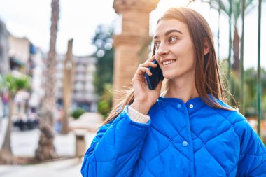 Beyaz bir kadın gülümsüyor ve caddede akıllı telefondan konuşuyor.