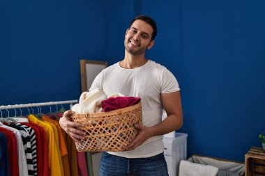 Çamaşır odasında çamaşır sepetini tutan kendine güvenen İspanyol genç adam.