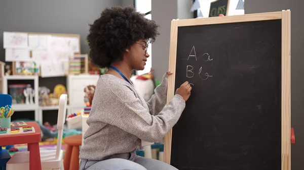 アフリカ系アメリカ人の女性教師が幼稚園で黒板に書く — ストック写真