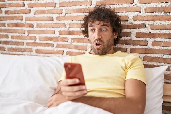침대에서 스마트폰을 사용하는 히스패닉 청년은 놀라움 과놀라움 수없는 얼굴에 벌렸다 — 스톡 사진