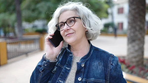 Middle age woman with grey hair speaking on the phone at park