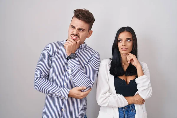白い背景の上に立っている若いヒスパニック系のカップルは 質問を心配し 心配し 顎に手で緊張 — ストック写真