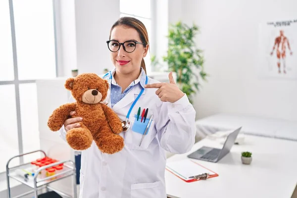 Young Hispanic Pediatrician Woman Holding Teddy Bear Clinic Pointing Finger — Stock Photo, Image