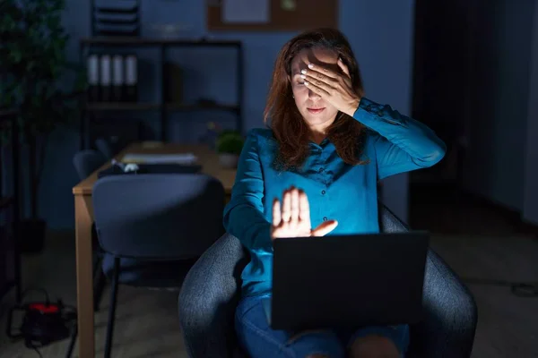 Brunette woman working at the office at night covering eyes with hands and doing stop gesture with sad and fear expression. embarrassed and negative concept.