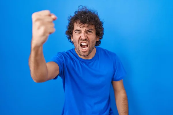 青の背景に立っているヒスパニック系の若者は怒りながら怒りで叫んでいる間 拳をフラストレーションと激怒を上げ怒っています 怒りと攻撃的な考え方 — ストック写真