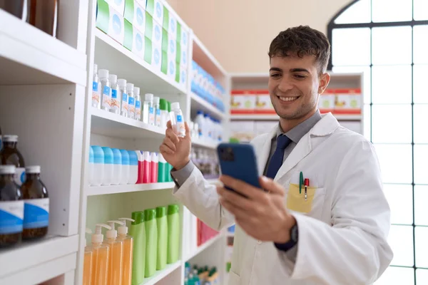 Young Hispanic Man Pharmacist Using Smartphone Holding Medication Bottle Pharmacy — Stock fotografie