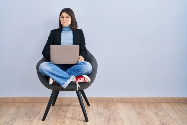 若いヒスパニック系の女性が面白い顔でコンピュータのラップトップの頬をむき出しの使用して椅子に座っている 口は空気で膨らみ狂気の表情で — ストック写真