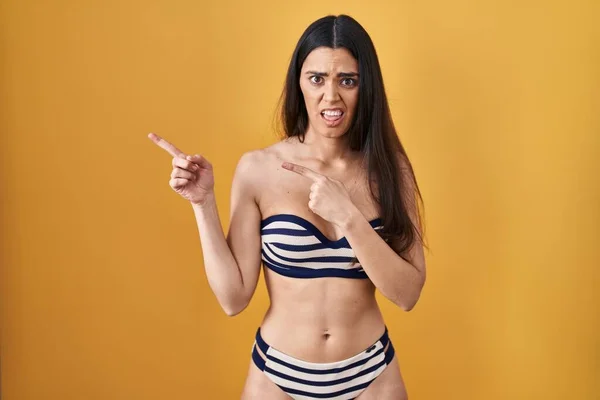 Mujer Morena Joven Con Bikini Sobre Fondo Amarillo Señalando Lado — Foto de Stock
