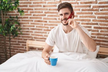 Kafkasyalı genç adam akıllı telefonda konuşuyor. Yatak odasında kahve içiyor.