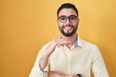 İspanyol genç adam iş kıyafetleri ve gözlük takıyor. Elleriyle işaret ediyor. Ölçü sembolü. Kameraya bakıp gülümsüyor. ölçüm kavramı. 