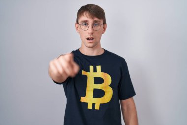 Bitcoin tişörtlü, beyaz tenli, sarışın bir adam kameraya kızgın ve sinirli olduğunu gösteriyor. 