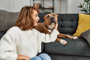 Beyaz kadın gülümsüyor. Kendine güvenen, kucaklayan köpek evde yerde oturuyor.