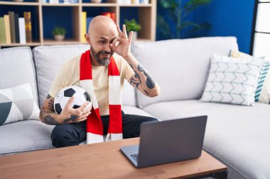 Dövmeli İspanyol bir adam futbol maçı seyrediyor. Futbol topu dizüstü bilgisayarda, gülümsüyor ve gülümsüyor. Tamam. 