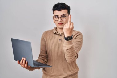 Non binary person using computer laptop showing middle finger, impolite and rude fuck off expression 