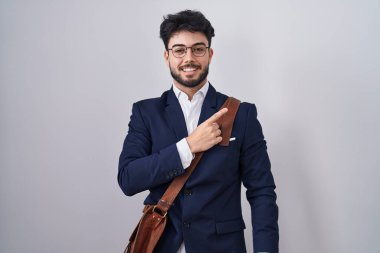 Hispanic man with beard wearing business clothes cheerful with a smile on face pointing with hand and finger up to the side with happy and natural expression 
